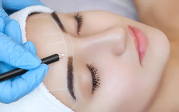 Permanent make-up for eyebrows of beautiful woman with thick brows in beauty salon. Closeup beautician doing  tattooing eyebrow.