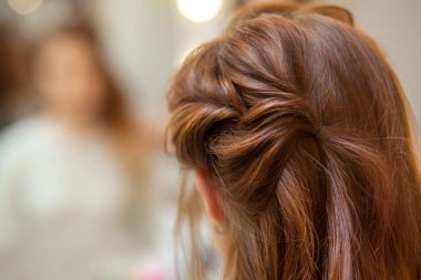 Güzel, kızıl saçlı uzun saçlı bir kız, kuaför bir güzellik salonunda Fransız örgüsü örüyor. Profesyonel saç bakımı ve saç modelleri.
