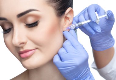 Doktor kozmetik uzmanı, güzellik salonundaki genç ve güzel bir kadının kulak memesinde pürüzleri gidermek ve cilt sarkıklığına karşı yüz enjeksiyonlarını yenileyen bir prosedür uyguluyor..