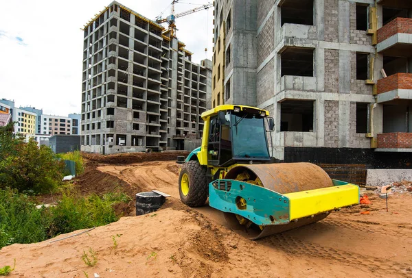 a tractor roller compacts the ground for the construction of a new road against the background of a new house