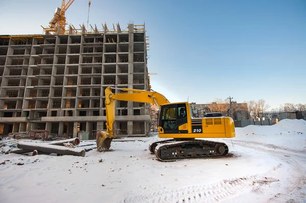 Yellow excavator on the background of a new monolithic house under construction in winter — Stock Image Yellow Excavator Background New Monolithic House Construction Winter Royalty Free Stock Images