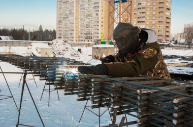 Bir inşaat işçisi, monolitik bir ev için metal bir çerçeve kaynak yapar.