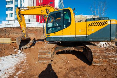 Sarı kazıcı kışın yeni bir evin arka planında bir inşaat alanında.