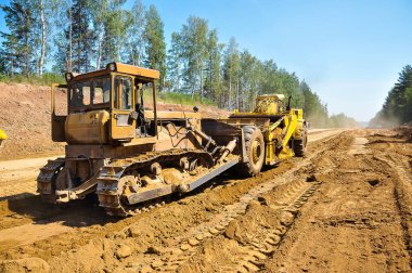 Traktör kazıyıcısı yeni yolun zeminini düzleştiriyor. Yeni bir yol inşaatı