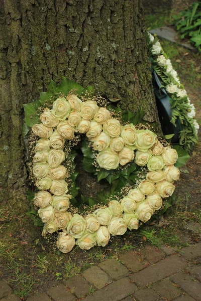 Heart shaped sympathy flowers  or funeral flowers near a tree, white roses