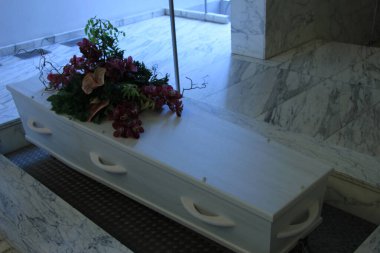 Krematoryumda cenaze çiçekleri olan beyaz bir tabut.