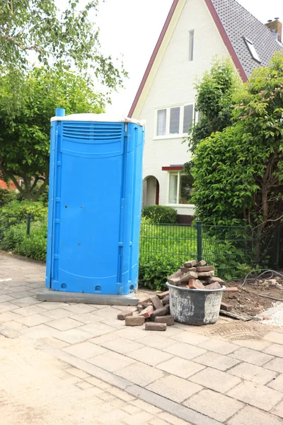 A blue, portable toilet cabin near a construction site