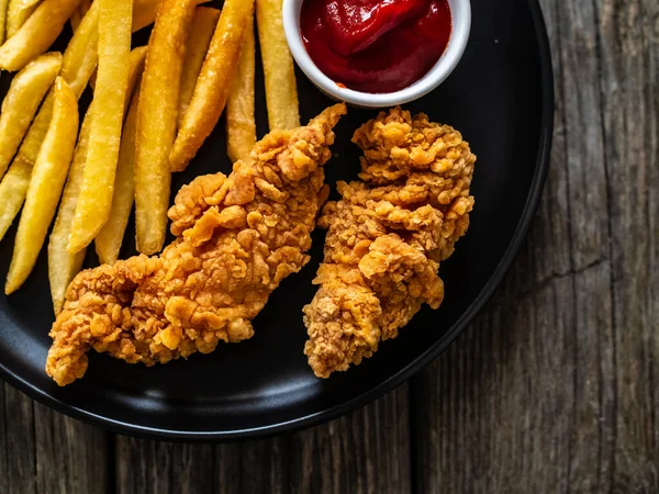 Fried breaded chicken nuggets with French fries and ketchup on wooden table