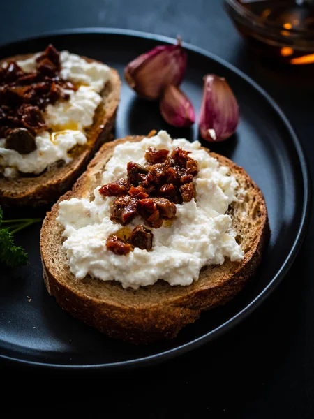 Breakfast - cottage cheese, bread, bruschetta and vegetables on black wooden table