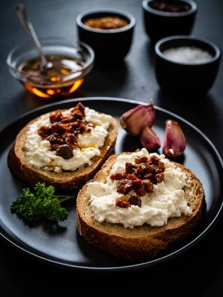 Breakfast - cottage cheese, bread, bruschetta and vegetables on black wooden table