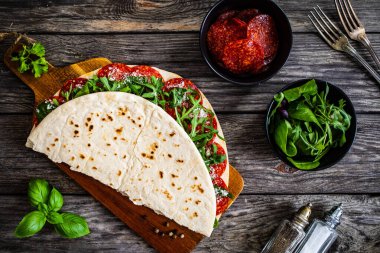 Italian piada wraps - piadina stuffed with fresh vegetable leaves and salami sausage on wooden table  clipart