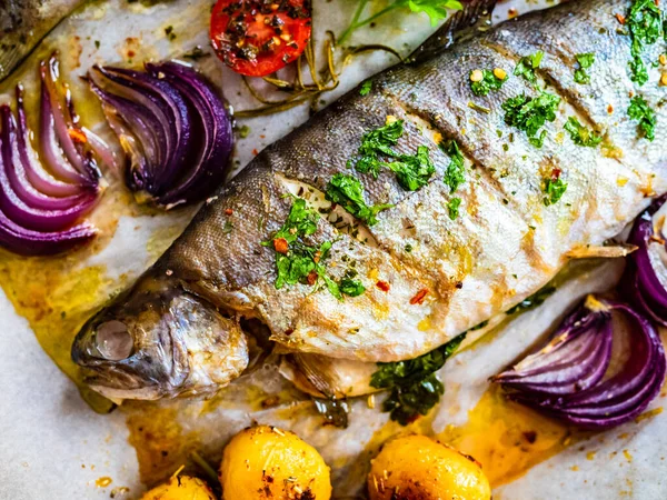 Sheet pan dinner - roasted whole trouts with lemon ,rosemary, tomatoes, red onion and potatoes on cooking pan on wooden table