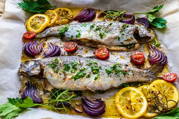 Sheet pan dinner - roasted whole trouts with lemon ,rosemary, tomatoes, red onion and potatoes on cooking pan on wooden table