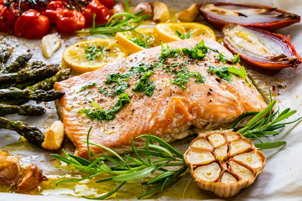 Sheet pan dinner - roasted salmon steak with asparagus, lemon ,rosemary, tomatoes, onion and garlic on cooking pan on wooden table