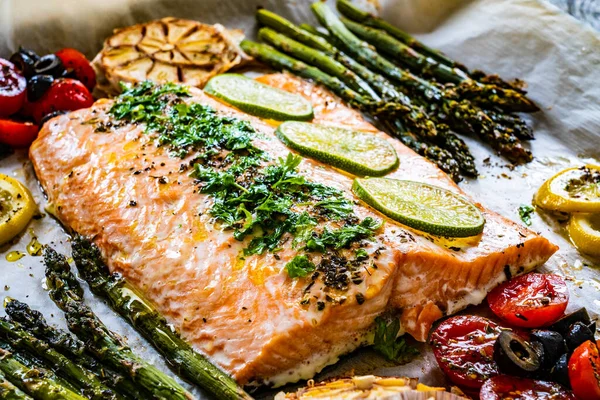Sheet pan dinner - roasted salmon steak with asparagus, lemon ,rosemary, tomatoes, onion and garlic on cooking pan on wooden table