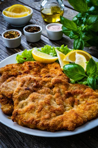 Breaded fried pork chop with lemon and fresh vegetables on wooden table