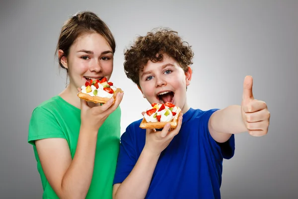 Meisje en jongen eten taart met vruchten en room — Stockfoto
