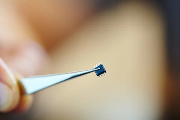 Mão segurando microchip com pinças — Fotografia de Stock