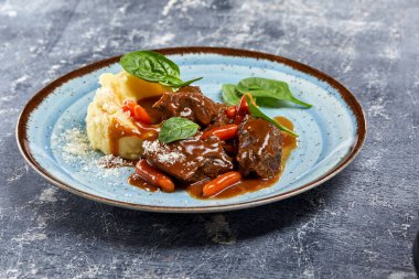 Beyaz tabakta patates püresi ve sebzeli sığır eti. 