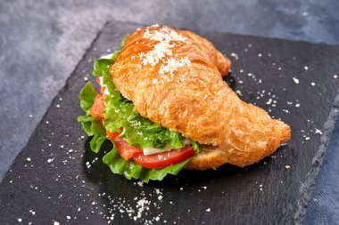 Karanlık tahtada jambonlu ve sebzeli kruvasan, yakın görüş.