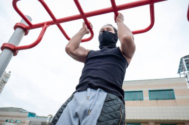 Adam karantinada siyah bir tişört ve maskeyle parmaklıklara tırmanıyor.