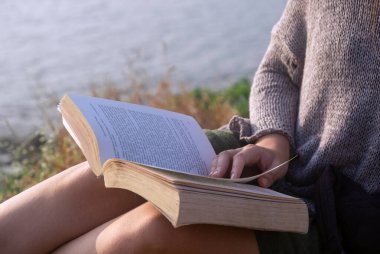 Açık havada otururken kitap okuyan genç kadın, yakın çekim