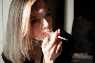 Pencerenin yanında sigara içen genç kadının yakın çekimi.