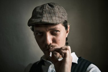 Genç adam sigara içiyor, duman üflüyor, retro tarzı giyinmiş, bereli, sinematik bir çekim, büyük bir yakın çekim