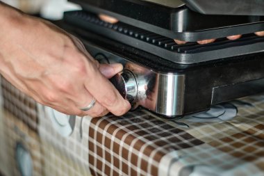 Adamın eli ızgaraya çiğ sosis serer, yakın çekim.