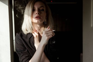 Pencerenin yanında sigara içen genç kadının yakın çekimi.