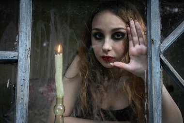 Güzel üzgün genç kız elinde mumla pencereden dışarı bakıyor, kitap kapağı için iyi.