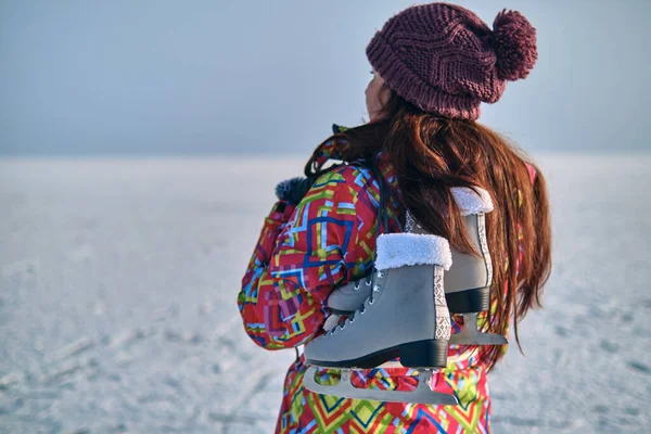 一位穿着滑雪服的妇女在结冰的湖上滑过之后 肩膀上抱着冰鞋 望着远方 — 图库照片