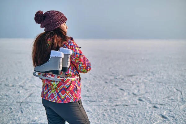 一位穿着滑雪服的妇女在结冰的湖上滑过之后 肩膀上抱着冰鞋 望着远方 — 图库照片