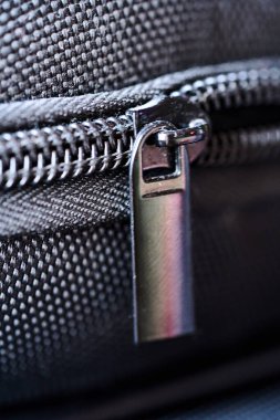 Siyah kumaş yüzeyinde bir fermuar gösterilir. Yakın çekim, kumaşın metal çekimini ve dikişini vurguluyor. Fermuardan yansıyan ışık..