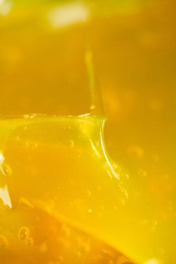 Parlak sarı bir maddenin yakın çekim görüntüsü pürüzsüz dokusunu ve parlak yüzeyini gösterir. Işık şeffaf bölgelerinden yansıyor..