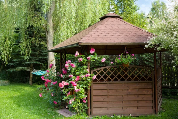 Outdoor wooden gazebo with roses and summer landscape background — Stock Photo, Image