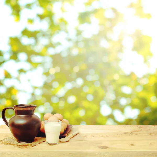 Table with a jug, milk and eggs on spring background — Stock Photo, Image