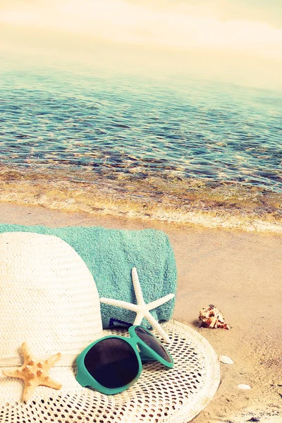 Sombrero de paja, gafas de sol, toalla y estrella de mar en la playa de arena . —  Fotos de Stock