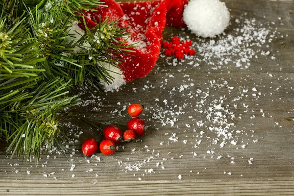 Pohon cemara Natal dengan topi merah dan salju di latar belakang kayu — Stok Foto