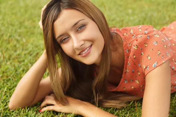 草の上に横たわると、カメラを見ながら笑顔の美少女 — ストック写真