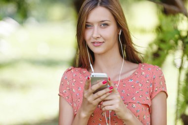 Güzel kız bir yaz ormanda iken beyaz telefon ile müzik dinlemek