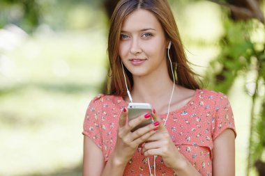 Güzel kız bir yaz ormanda iken beyaz telefon ile müzik dinlemek