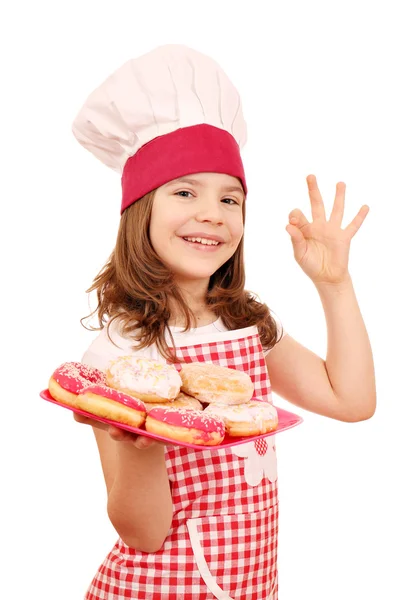 Feliz niña cocinera con rosquillas dulces y señal de mano ok — Foto de Stock