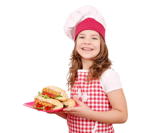 Happy little girl cook with hot dogs on plate — Stock Photo, Image