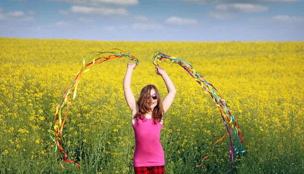 Glückliches kleines Mädchen winkt mit bunten Bändern auf dem Feld — Stockfoto