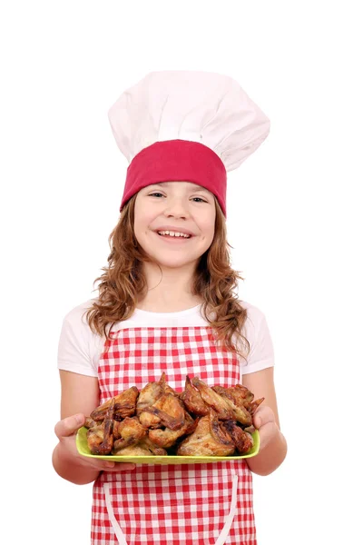 Happy little girl cook with chicken wings on plate — Stock Photo, Image