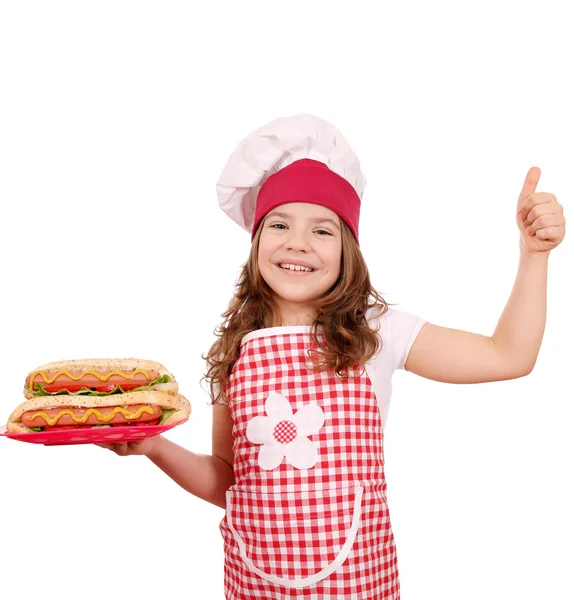 Happy little girl cook with hot dogs and thumb up — Stock Photo, Image