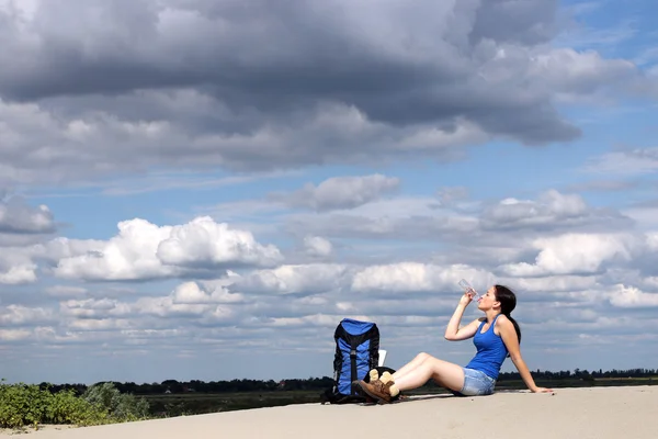 Дівчина пішохід сидить на піску і п'є воду — стокове фото
