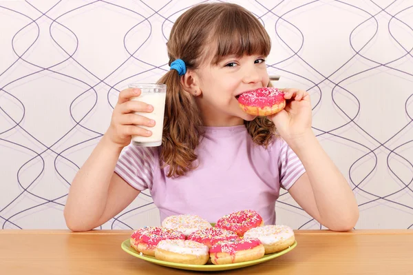 Hladová malá holčička jíst koblihy a pít mléko — Stock fotografie