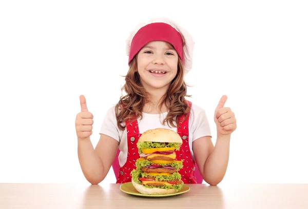 Happy little girl cook with big hamburger and thumbs up — Stock Photo, Image